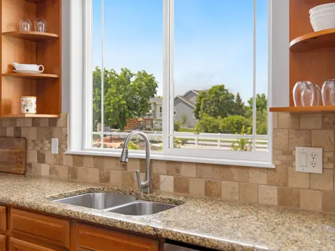 A kitchen sink with a pull-down faucet under a window looking onto a green yard