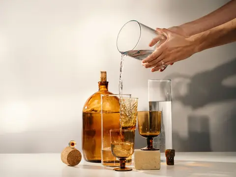 Hands pouring water from one glass into another in soft light