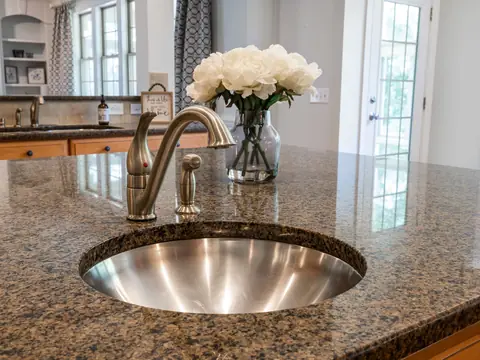 A round steel sink with a faucet and a side sprayer in a granite counter