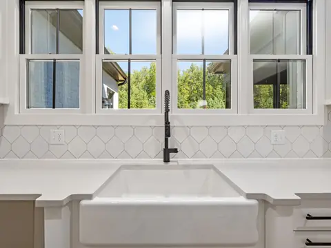 A white farmhouse sink under a row of windows in a bright kitchen
