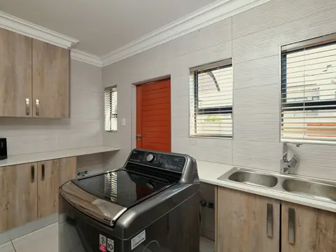 A bright room with a washing machine beside a double sink and wooden cabinets