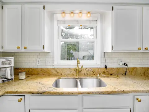A bright kitchen with a double sink under a window and marble counters