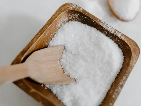Coarse white salt in a wooden bowl with a wooden scoop