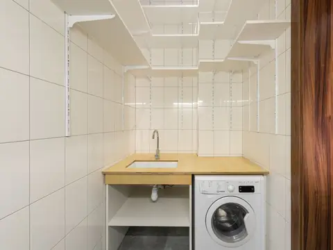 A white tiled utility room with a small sink, open shelves and a washing machine