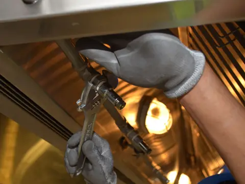 Gloved hands working a wrench on a pipe fitting