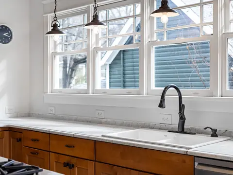 A black faucet over a white sink under tall windows