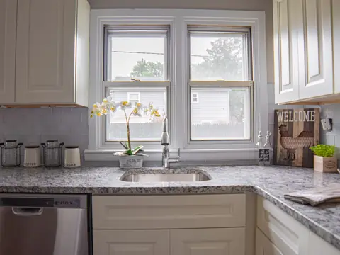 A bright kitchen with a sink under twin windows and granite counters