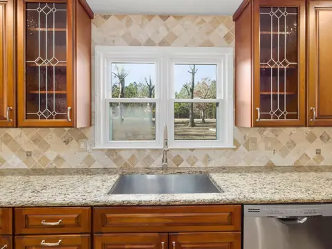 A kitchen sink under a window framed by wooden cabinets
