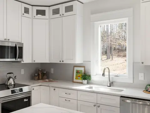 A white kitchen with the sink under a window and a kettle on the stove