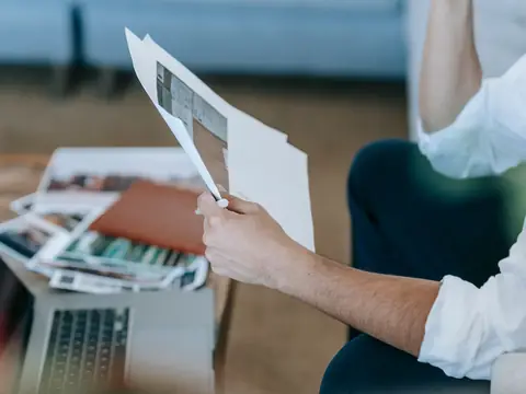 Hands holding printed pages over a table with a laptop