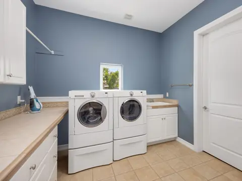 A laundry room with a washer and dryer on pedestals and white cabinets