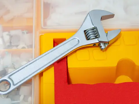 An adjustable wrench resting on a bright yellow and red tool case