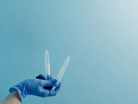 A gloved hand holding up two small sample tubes against a blue wall