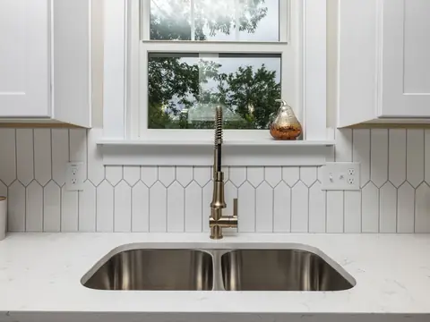A white kitchen with a steel double sink and a tall faucet under a window