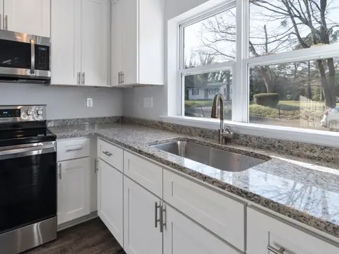 A bright kitchen with a steel sink under a wide window and granite counters