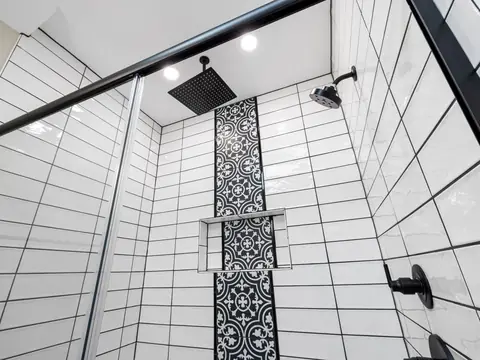A walk-in shower with black fixtures and a patterned tile wall