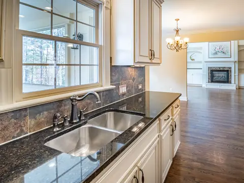 A kitchen with a steel sink under a window and granite counters