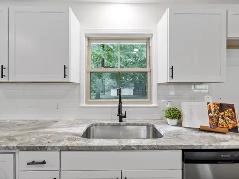 A white kitchen with a black faucet over a steel sink under a window