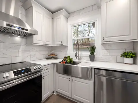 A white kitchen with a farmhouse sink, a steel range and a hood