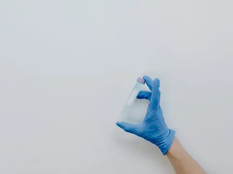 A gloved hand holding a small sample tube against a white wall