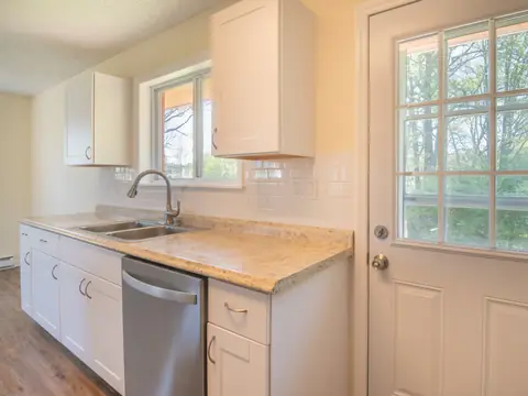 A sunlit white kitchen with the sink under a window