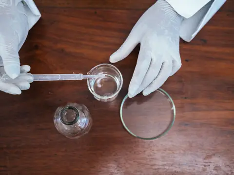 Gloved hands drawing a small sample of water with a pipette