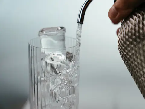Water pouring from a black spout into a tall ribbed glass