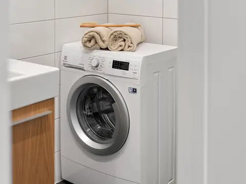 A front-load washing machine with folded towels on top in a white room