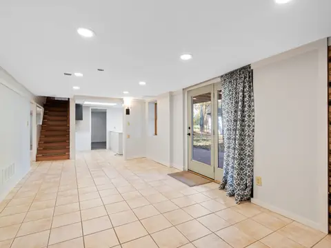 A bright, empty finished basement with a tile floor, stairs and glass doors