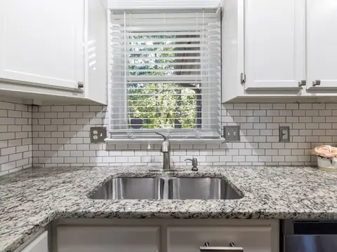 A kitchen with a double steel sink under a window and white cabinets