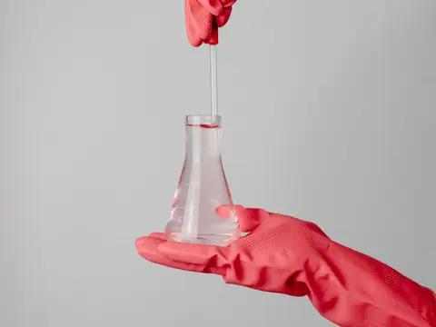 A gloved hand holding a glass flask of clear water for testing