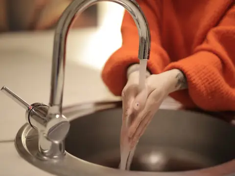 Water running from a chrome kitchen faucet into a round steel sink