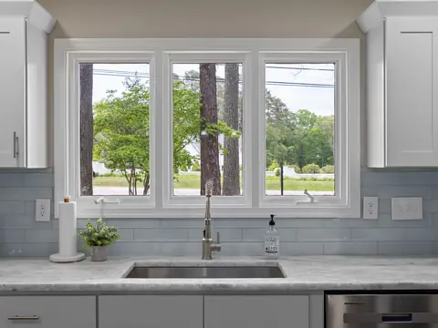 A bright kitchen with the sink and faucet under a wide window looking onto trees