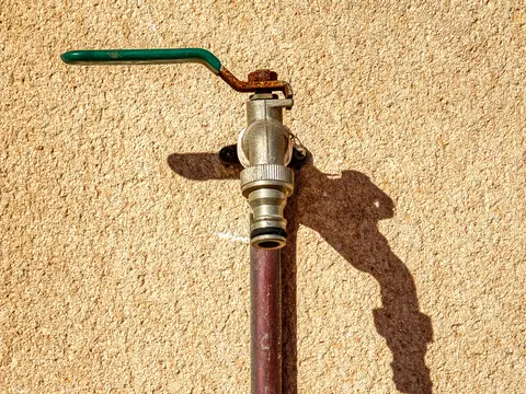 An outdoor tap with a green handle on a textured wall